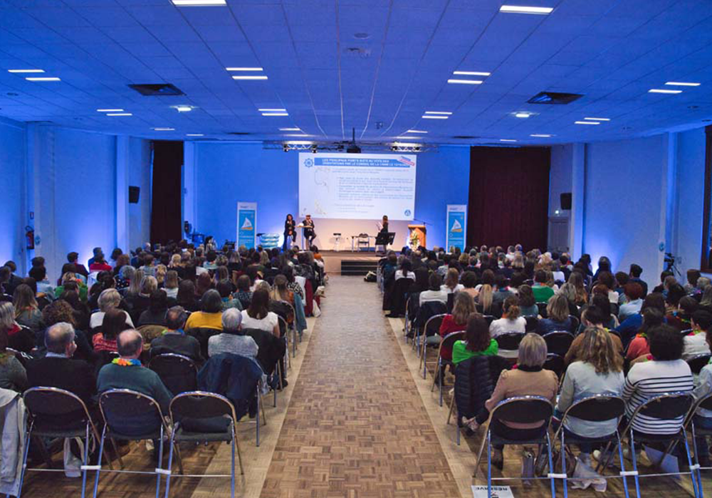 Une salle d'assemblée générale où l'on aperçoit les 300 collaborateurs assis de dos face à la scène où la présentation de l'AG 2023 est donnée